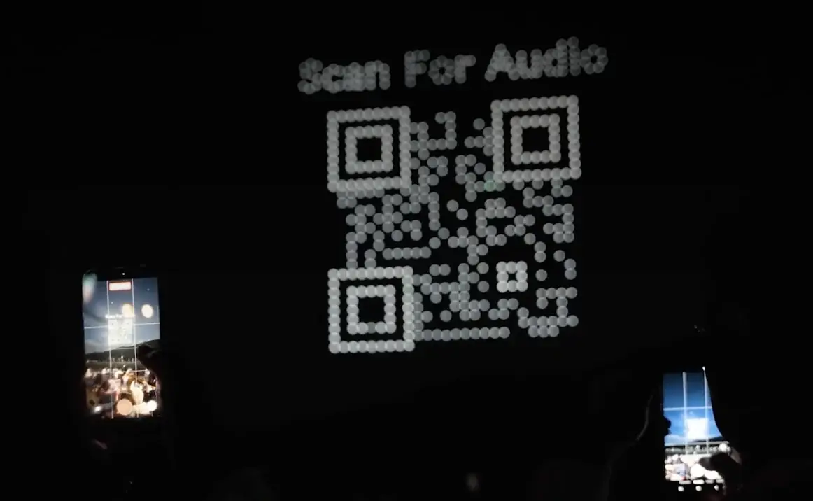 Drones forming a scannable Scan For Audio QR code over a night audience filming on their phones
