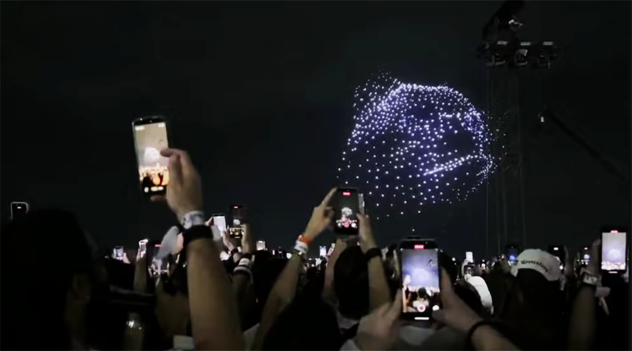 Crowd at Shakira's Copacabana concert holding up dozens of phones to film the drone show forming overhead