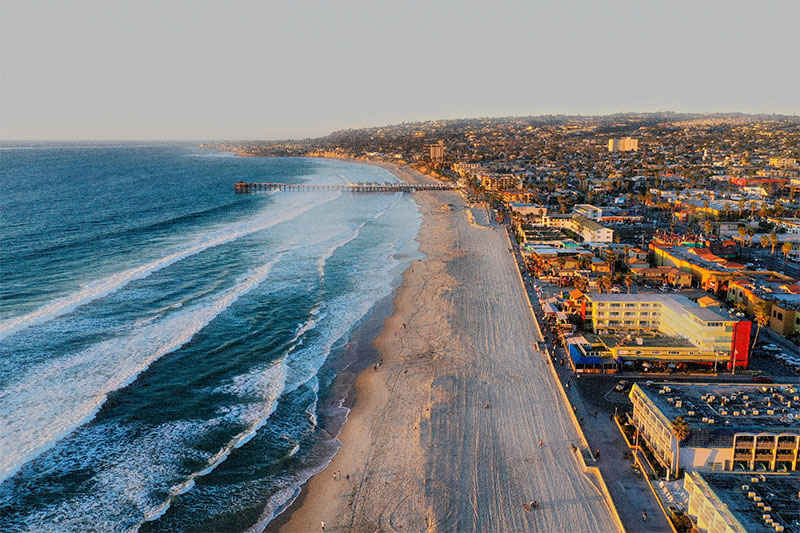 Scenic aerial view of the San Diego coastline where drone flights are allowed, showing the beach, ocean, and pier at sunset by Creative Skies Drone Light Shows.